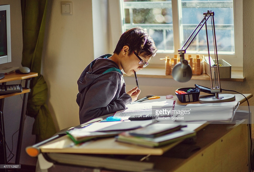 Boy sitting at desk with books and work.