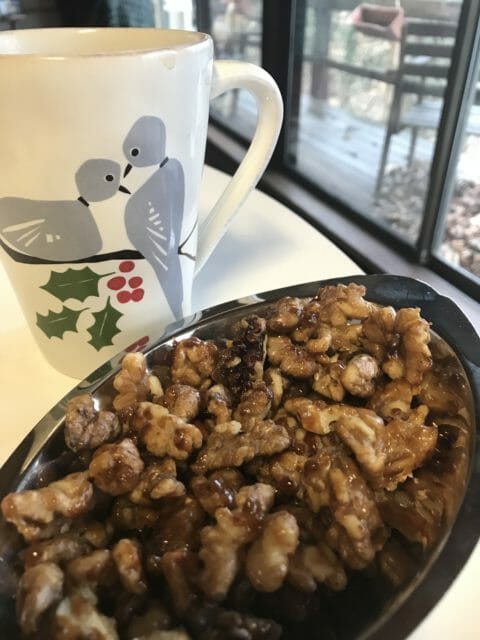 Candied walnuts in a silver dish next to a cup of coffee.