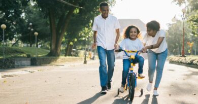 man standing beside his wife teaching their child how to ride bicycle