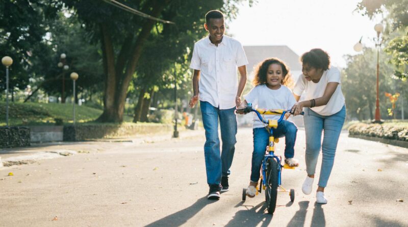 man standing beside his wife teaching their child how to ride bicycle